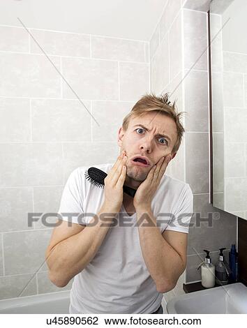 Stock Image - Portrait of man with hairbrush grimacing in bathroom. Fotosearch