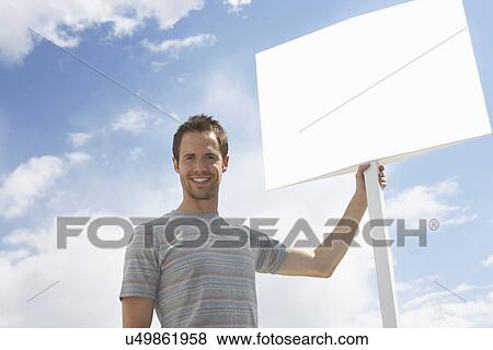 Portrait of man with standing by blank sign against cloudy sky View Large Photo Image Stock Photo - Portrait of man with standing by blank sign against cloudy sky. Fotosearch
