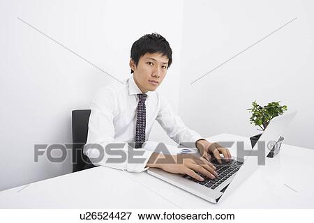 Stock Photo - Portrait of mid adult businessman using laptop at office desk. Fotosearch