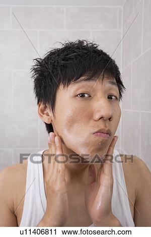 Stock Image - Portrait of mid adult man applying aftershave lotion in bathroom. Fotosearch