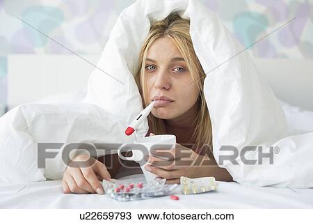 Portrait of sad woman with coffee mug taking temperature while wrapped in quilt on bed View Large Photo Image Stock Image - Portrait of sad woman with coffee mug taking temperature while wrapped in quilt on bed. Fotosearch