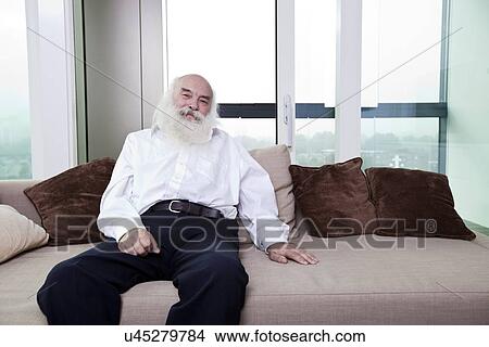 Picture - Portrait of senior man relaxing on sofa in apartment. Fotosearch