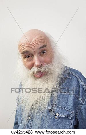 Stock Photo - Portrait of senior man sticking out tongue over gray background. Fotosearch