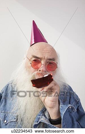 Portrait of senior man wearing party hat and red glasses while blowing horn against gray background View Large Photo Image Stock Image - Portrait of senior man wearing party hat and red glasses while blowing horn against gray background. Fotosearch