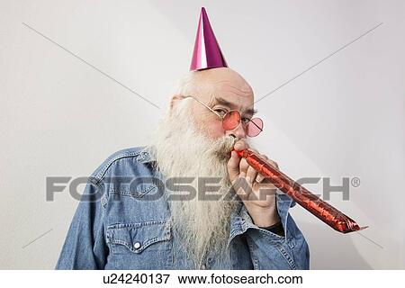 Portrait of senior man wearing party hat while blowing horn against gray background View Large Photo Image Stock Photo - Portrait of senior man wearing party hat while blowing horn against gray background. Fotosearch