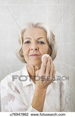 Stock Image - Portrait of senior woman applying face powder in bathroom. Fotosearch