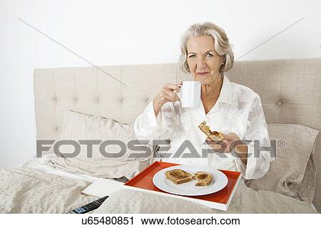 Stock Image - Portrait of senior woman having breakfast in bed. Fotosearch