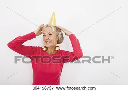 Stock Photo - Portrait of senior woman wearing party hat and Christmas ornaments over white background. Fotosearch