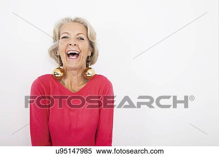Stock Photography - Portrait of senior woman wearing Christmas ornaments over white background. Fotosearch