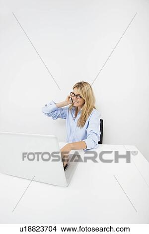 Picture - Portrait of smiling businesswoman answering smart phone in office. Fotosearch