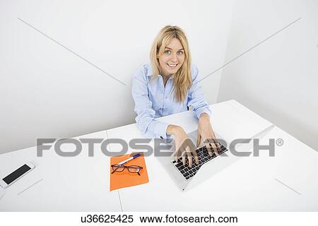 Stock Photography - Portrait of smiling businesswoman using laptop in office. Fotosearch
