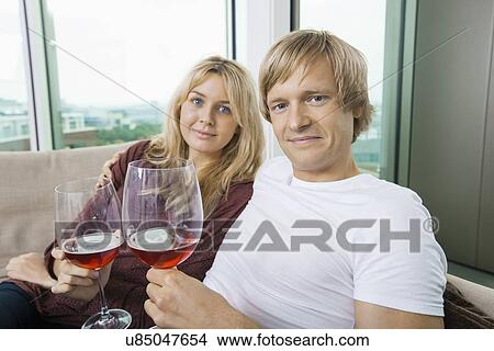 Portrait of smiling couple with wine glasses in living room at home View Large Photo Image Picture - Portrait of smiling couple with wine glasses in living room at home. Fotosearch