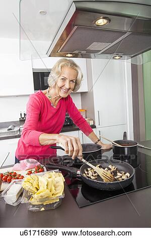 Stock Photo - Portrait of smiling senior woman cooking food in kitchen. Fotosearch
