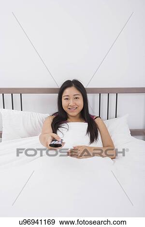 Portrait of smiling woman changing channels with remote control in bed View Large Photo Image Stock Photo - Portrait of smiling woman changing channels with remote control in bed. Fotosearch
