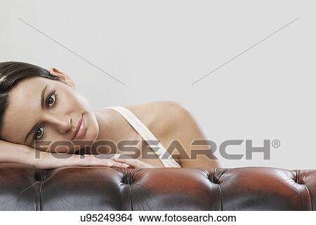 Portrait of woman leaning on sofa against gray background View Large Photo Image Picture - Portrait of woman leaning on sofa against gray background. Fotosearch
