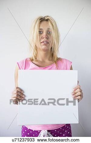 Stock Image - Portrait of woman suffering from cold holding blank placard against gray background. Fotosearch