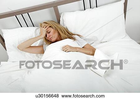 Stock Photo - Portrait of woman suffering from cold and headache in bed. Fotosearch
