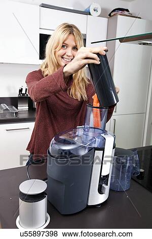 Stock Photo - Portrait of woman using juicer for juicing carrots at kitchen counter. Fotosearch