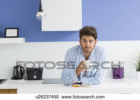 Portrait of young ill man holding coffee mug while leaning on kitchen counter View Large Photo Image Stock Image - Portrait of young ill man holding coffee mug while leaning on kitchen counter. Fotosearch