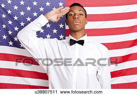 Stock Image - Portrait of young man saluting against American flag. Fotosearch