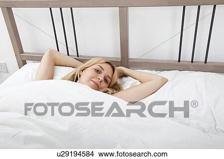 Picture - Portrait of young woman lying on bed. Fotosearch