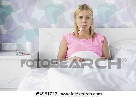 Portrait of young woman taking temperature with thermometer View Large Photo Image Stock Photo - Portrait of young woman taking temperature with thermometer. Fotosearch