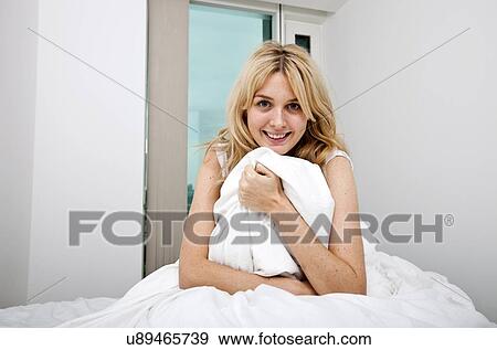 Stock Photo - Portrait of young woman with quilt sitting in bed. Fotosearch