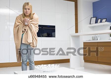 Stock Photography - Portrait of young woman wrapped in blanket holding coffee mug in house. Fotosearch