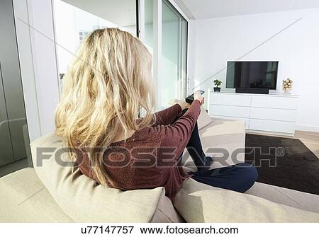 Rear view of young woman watching television on sofa at home View Large Photo Image Stock Photo - Rear view of young woman watching television on sofa at home. Fotosearch