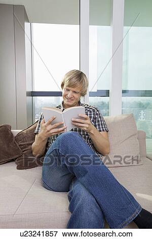 Relaxed mid-adult man reading book in living room at home View Large Photo Image Stock Photo - Relaxed mid-adult man reading book in living room at home. Fotosearch