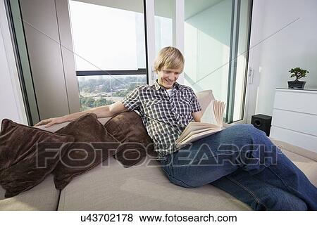 Relaxed mid-adult man reading book in living room at home View Large Photo Image Stock Photo - Relaxed mid-adult man reading book in living room at home. Fotosearch