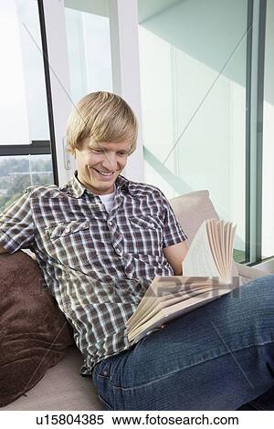 Relaxed mid-adult man reading book in living room at home View Large Photo Image Stock Photography - Relaxed mid-adult man reading book in living room at home. Fotosearch