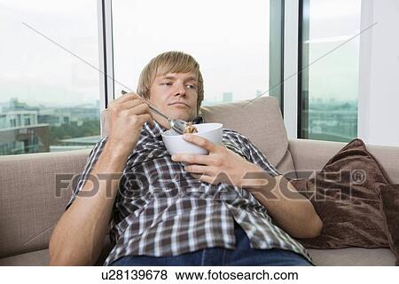 Relaxed mid-adult man with bowl of cereal in living room at home View Large Photo Image Stock Photo - Relaxed mid-adult man with bowl of cereal in living room at home. Fotosearch