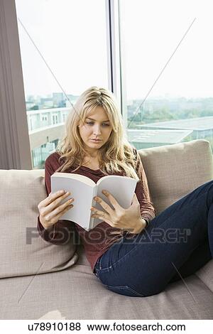 Relaxed young woman reading book in living room at home View Large Photo Image Stock Photo - Relaxed young woman reading book in living room at home. Fotosearch