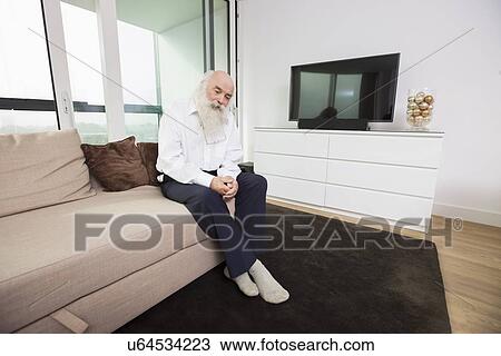 Sad senior man sitting on sofa in living room View Large Photo Image Stock Image - Sad senior man sitting on sofa in living room. Fotosearch