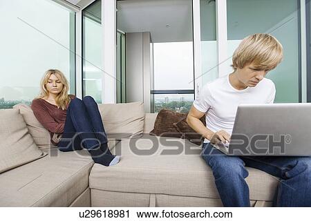 Sad woman beside man using laptop in living room at home View Large Photo Image Stock Image - Sad woman beside man using laptop in living room at home. Fotosearch