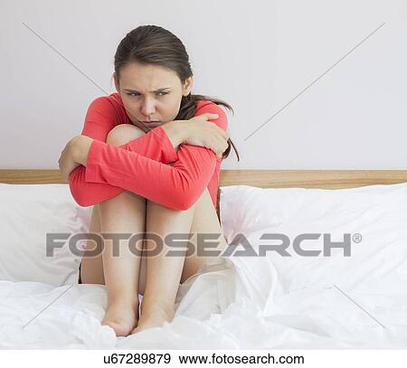 Stock Photo - Sad woman hugging knees on bed at home. Fotosearch