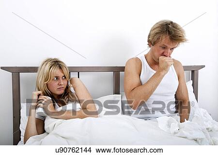 Picture - Scared woman looking at man coughing in bed. Fotosearch