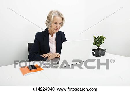 Senior businesswoman using laptop at desk in office View Large Photo Image Stock Image - Senior businesswoman using laptop at desk in office. Fotosearch