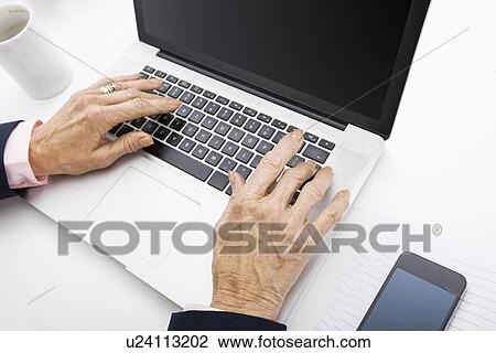 Stock Image - Senior businesswoman using laptop at office desk. Fotosearch