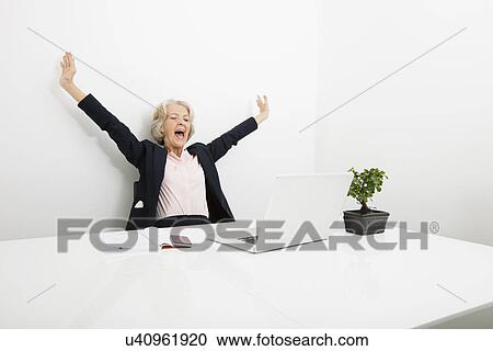 Stock Image - Senior businesswoman yawning while looking at laptop in office. Fotosearch