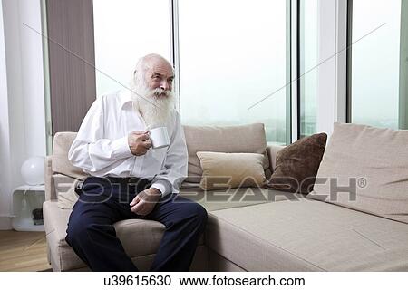 Senior man having coffee while sitting on sofa in apartment View Large Photo Image Stock Image - Senior man having coffee while sitting on sofa in apartment. Fotosearch