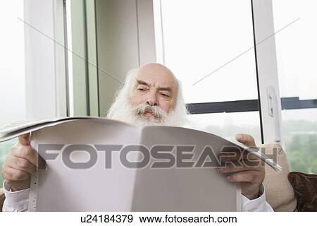 Stock Photo - Senior man reading newspaper in house. Fotosearch