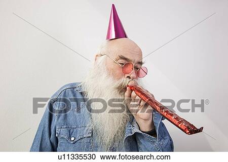 Senior man wearing party hat while blowing horn against gray background View Large Photo Image Stock Image - Senior man wearing party hat while blowing horn against gray background. Fotosearch