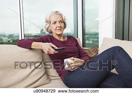 Senior woman using TV remote control on sofa at home View Large Photo Image Stock Photo - Senior woman using TV remote control on sofa at home. Fotosearch