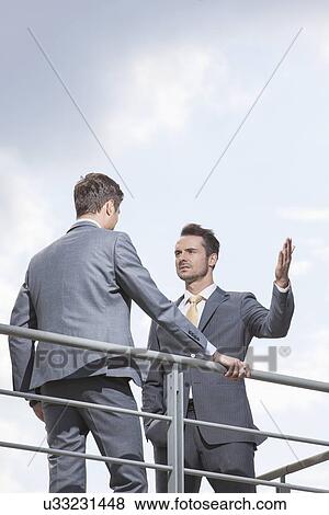 Serious businessman gesturing while looking at coworker against sky View Large Photo Image Stock Photo - Serious businessman gesturing while looking at coworker against sky. Fotosearch