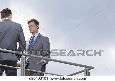 Stock Image - Serious businessman looking at coworker against clear sky. Fotosearch
