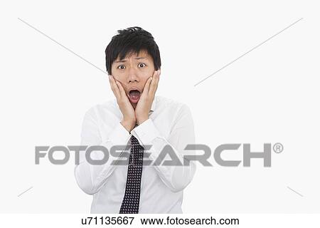 Stock Photo - Shocked mid adult businessman with hands on face over white background. Fotosearch
