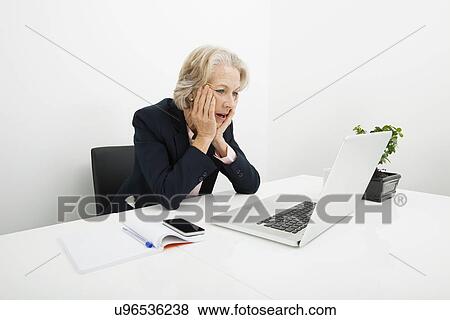 Shocked senior businesswoman using laptop at desk in office View Large Photo Image Stock Photo - Shocked senior businesswoman using laptop at desk in office. Fotosearch