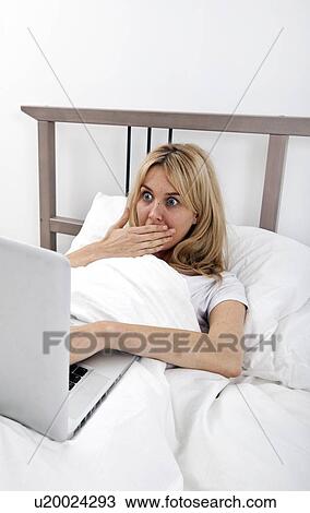 Shocked young woman looking at laptop in bed View Large Photo Image Stock Image - Shocked young woman looking at laptop in bed. Fotosearch